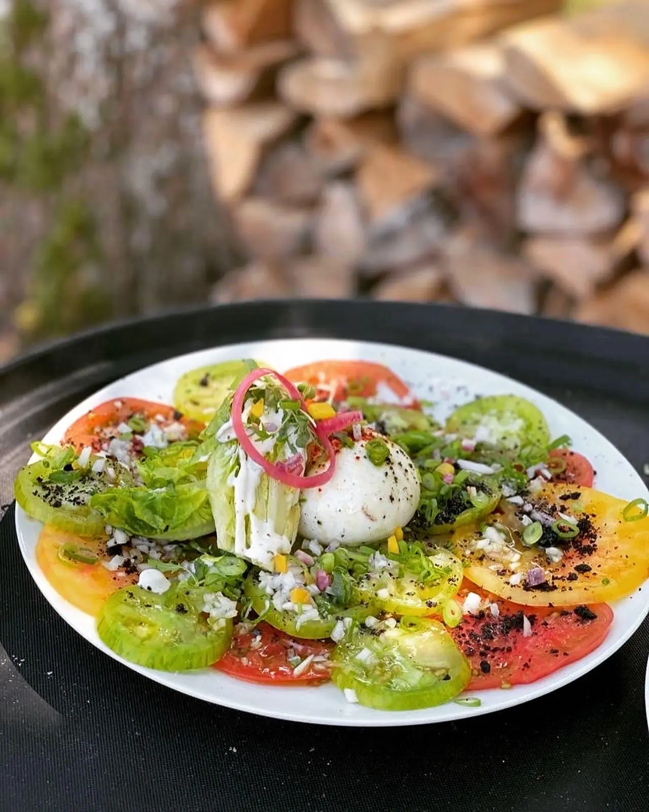Burrata posée sur un carpaccio de tomates anciennes de toutes les couleurs, pickles d'oignon rouge et herbes