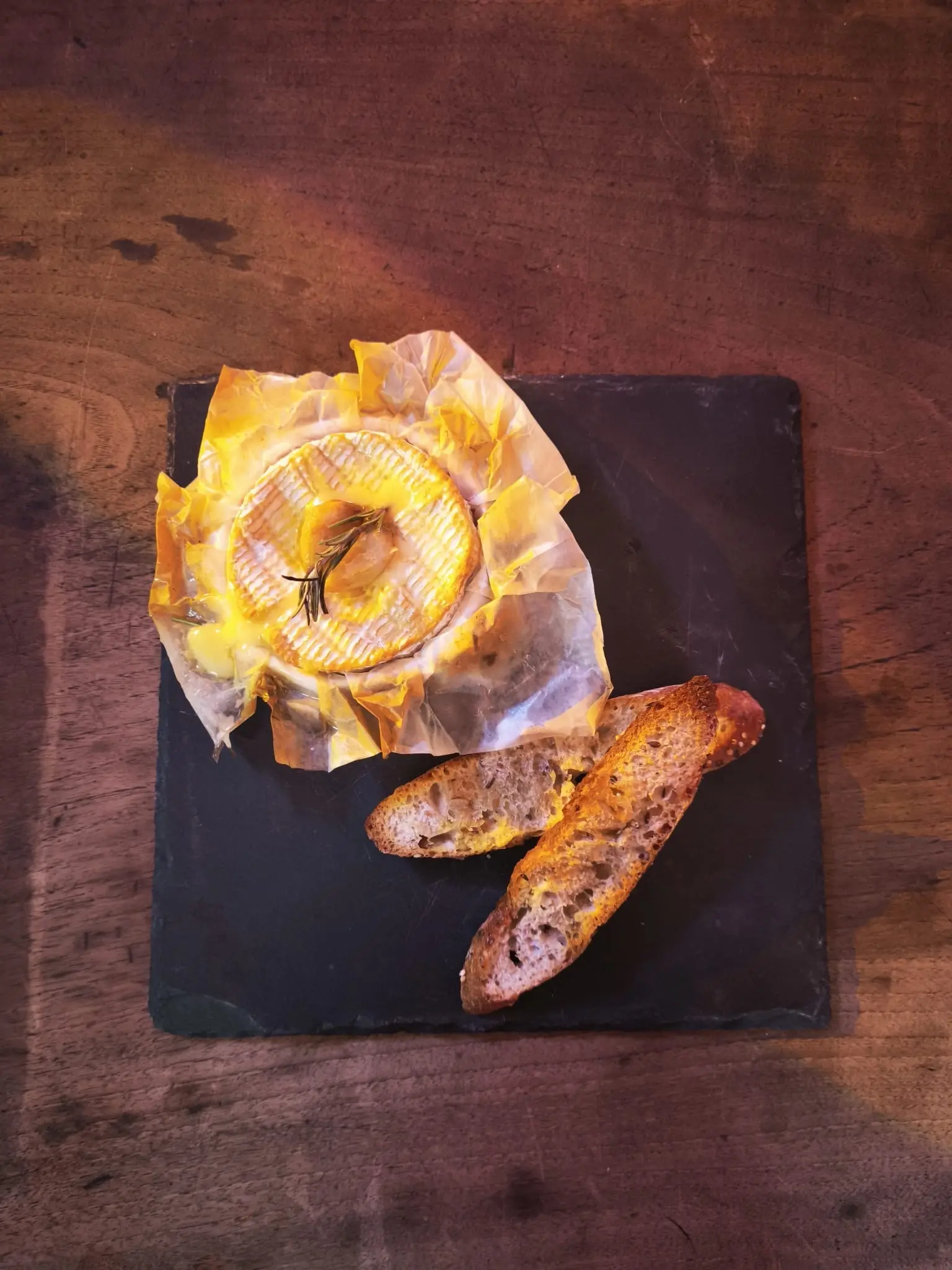 Camembert rôti au romarin dans son papier, servi sur ardoise avec des tartines grillées