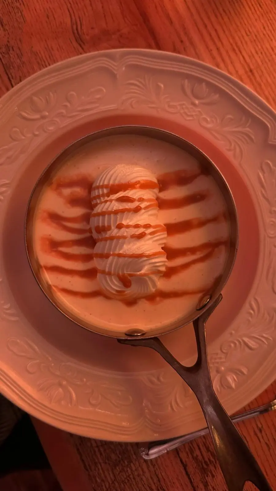 Meringue posée sur une crème, filets de coulis, servie dans une petite poêle en cuivre sur une assiette ancienne