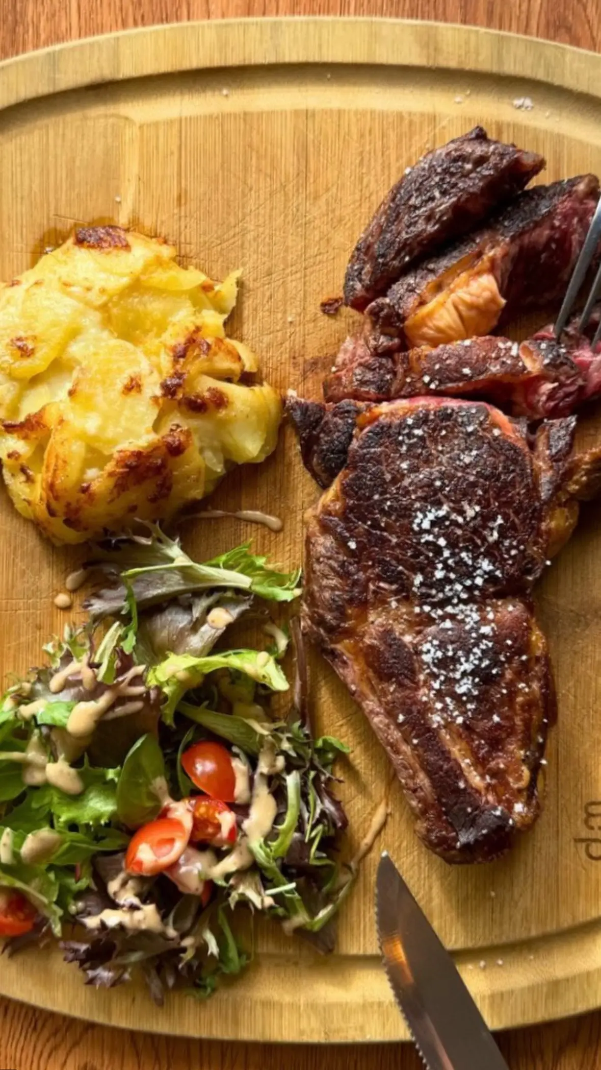 Entrecôte grillée à la fleur de sel, gratin de pommes de terre et salade sur une planche en bois