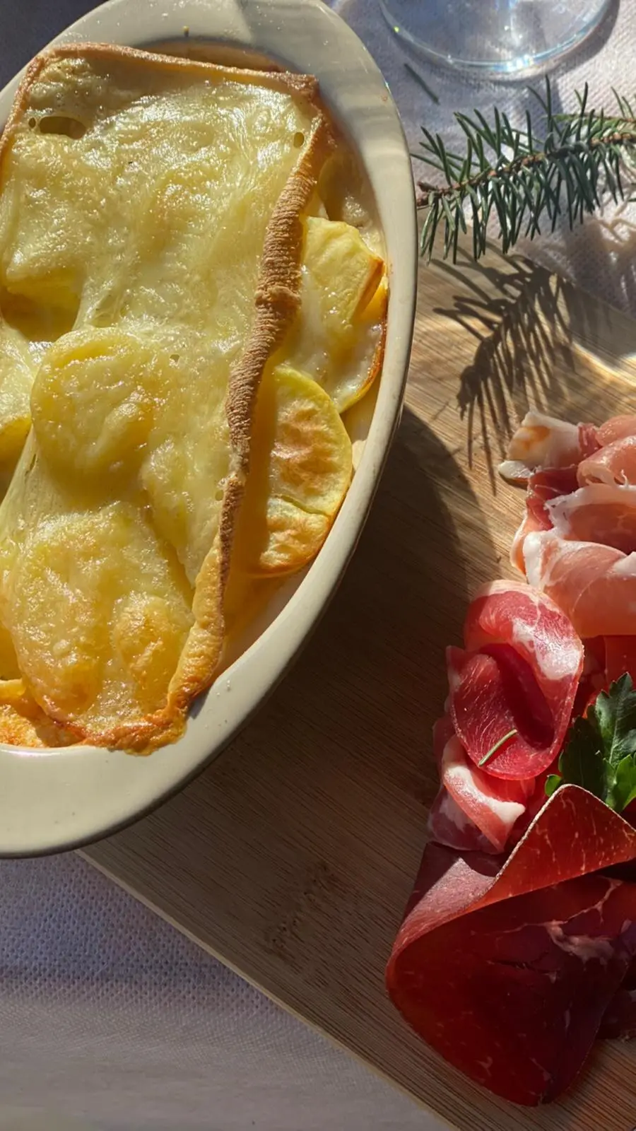 Plat à gratin de pommes de terre doré, servi avec des tranches de jambon cru et une branche de sapin