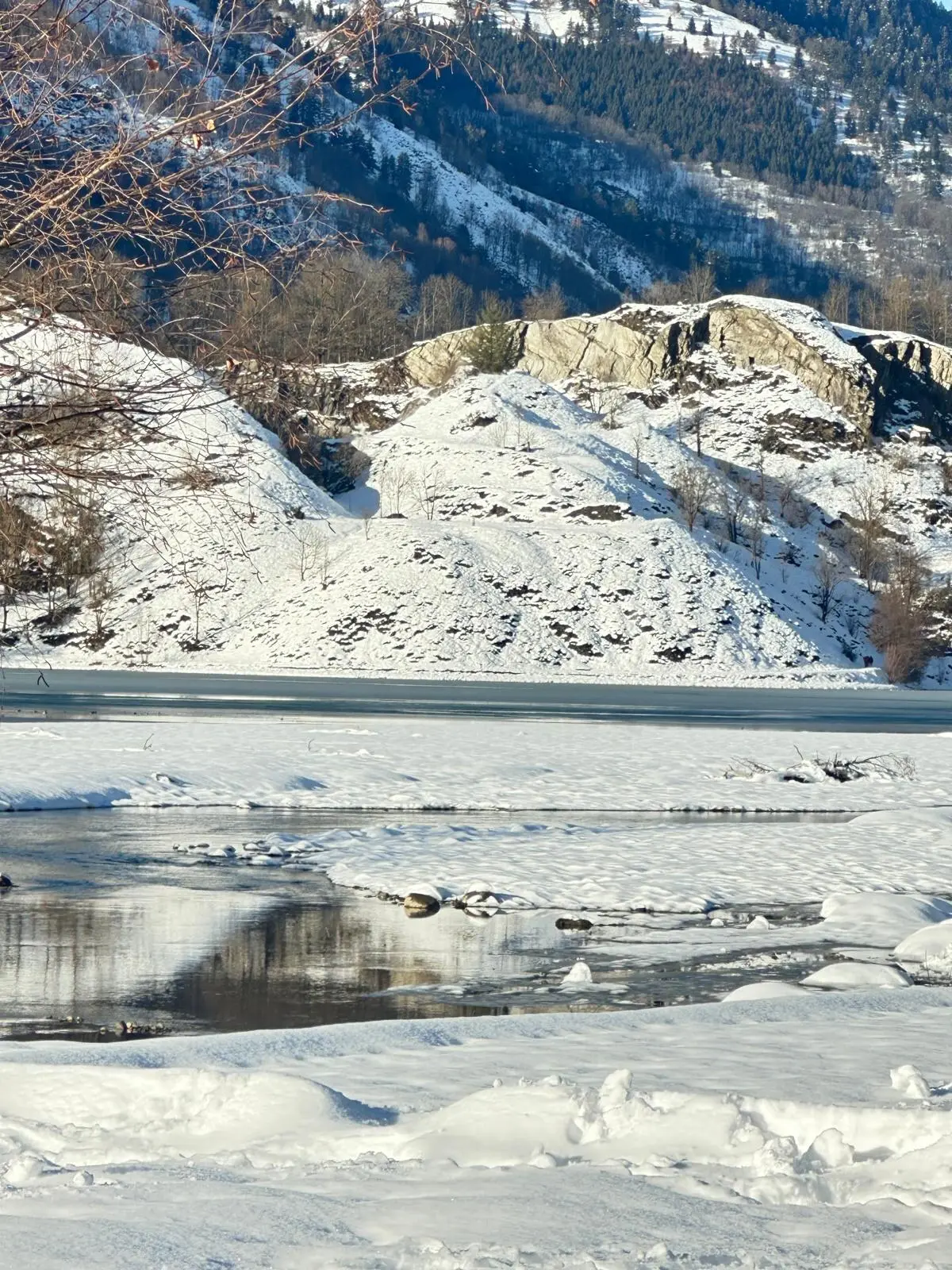 Le lac de Génos-Loudenvielle en partie gelé, berges enneigées et rochers au soleil