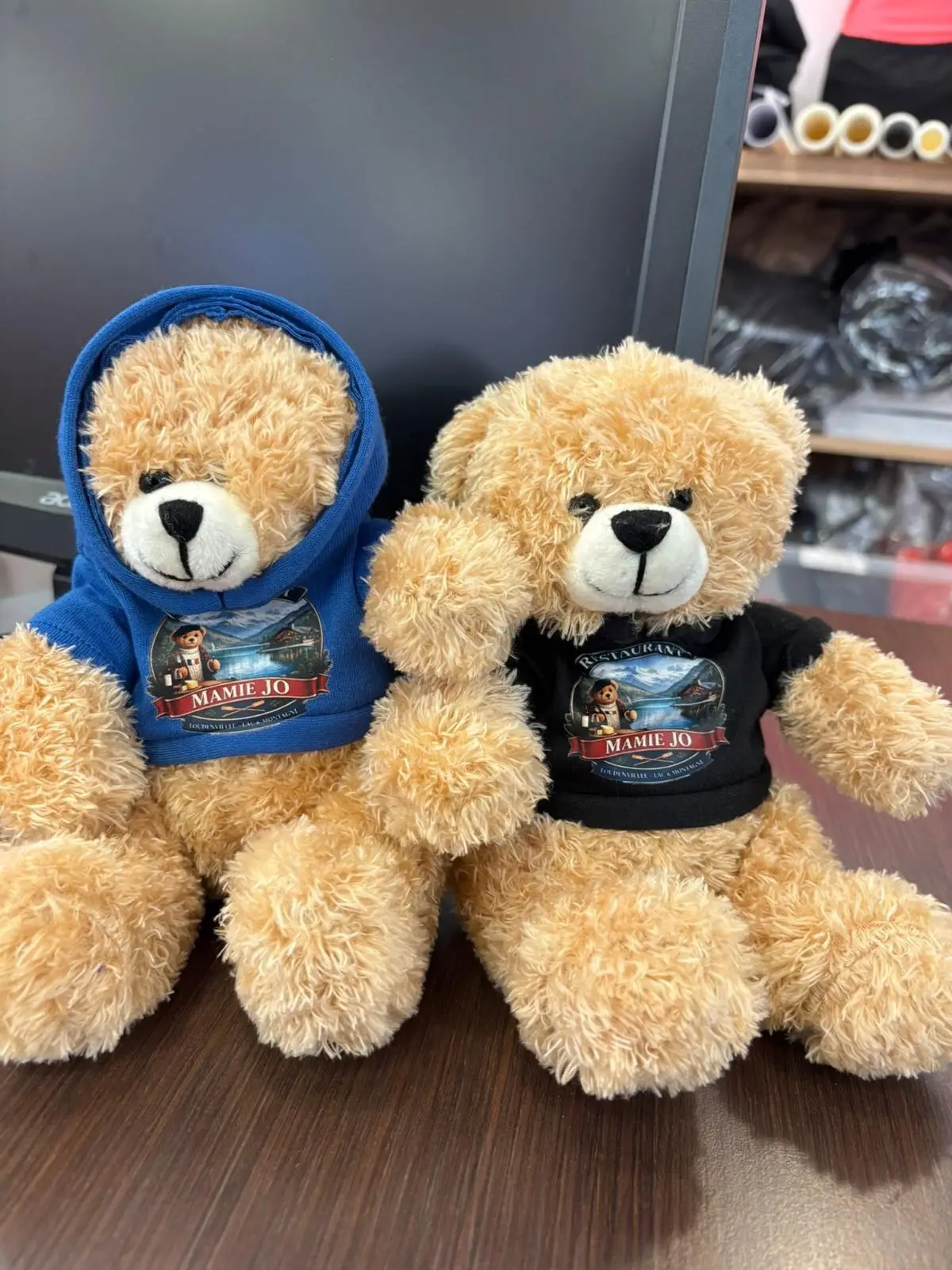 Deux oursons en peluche, l'un en sweat à capuche bleu, l'autre en t-shirt noir, tous deux à l'écusson Mamie Jo