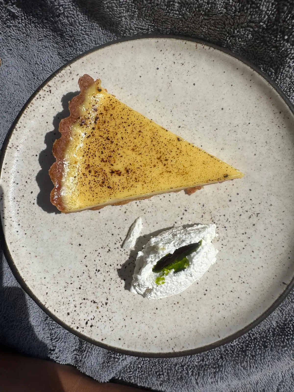 Part de tarte dorée et quenelle de crème, sur une assiette en grès