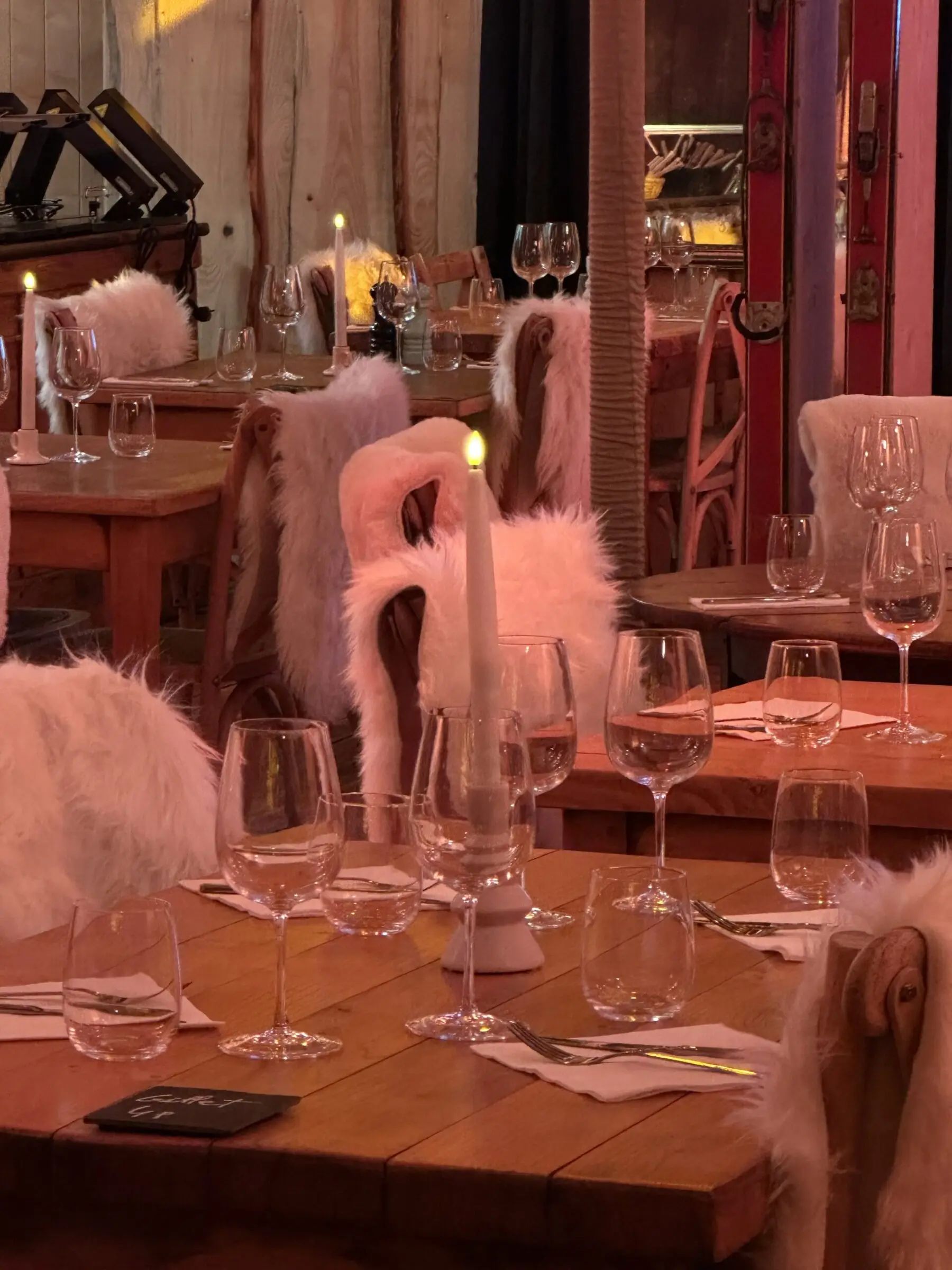La salle du chalet dressée pour le soir, bougies allumées, verres à pied et chaises couvertes de fourrure