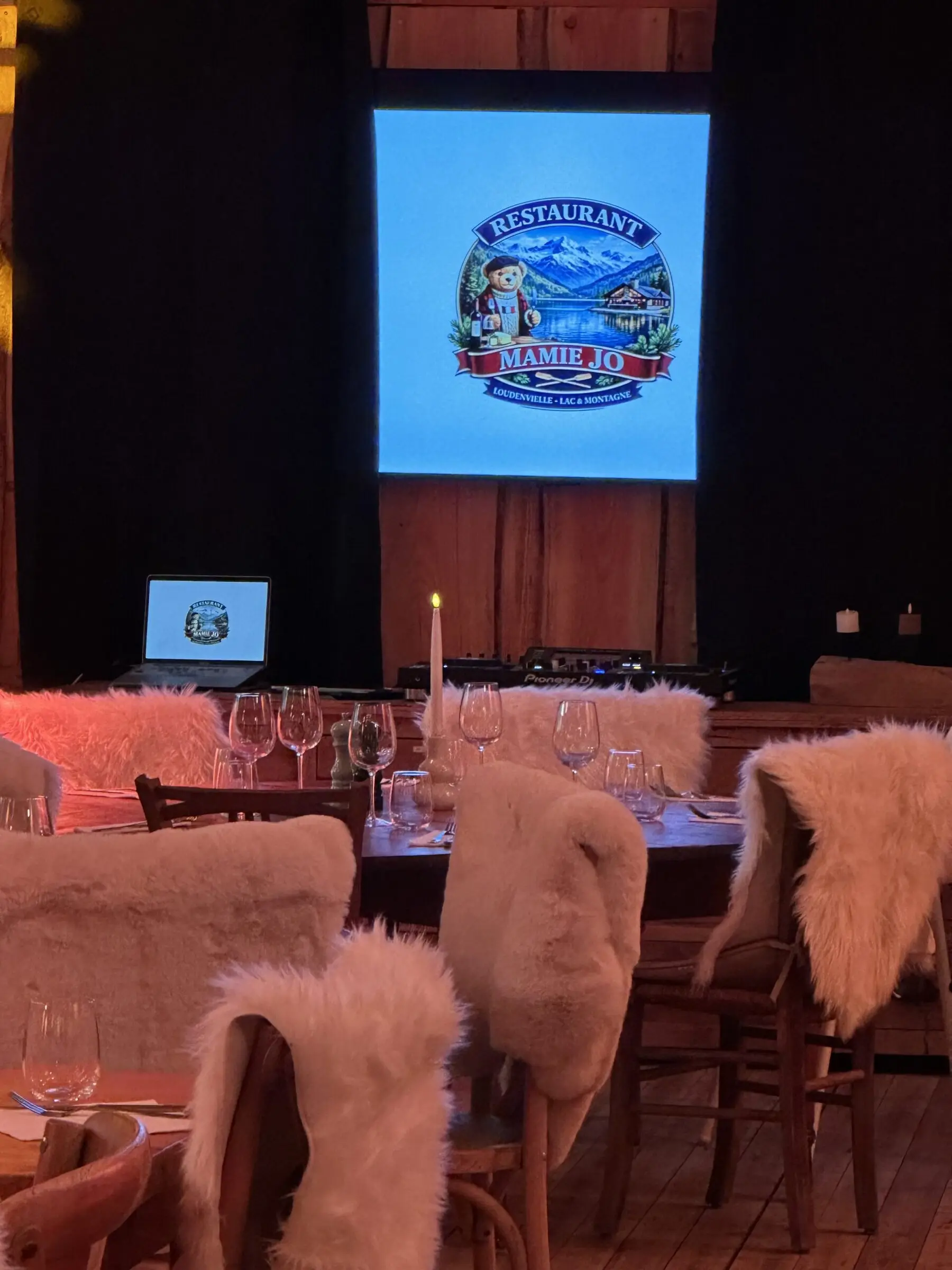 La salle du chalet dressée pour une soirée privée, chaises couvertes de fourrure, écran allumé au fond