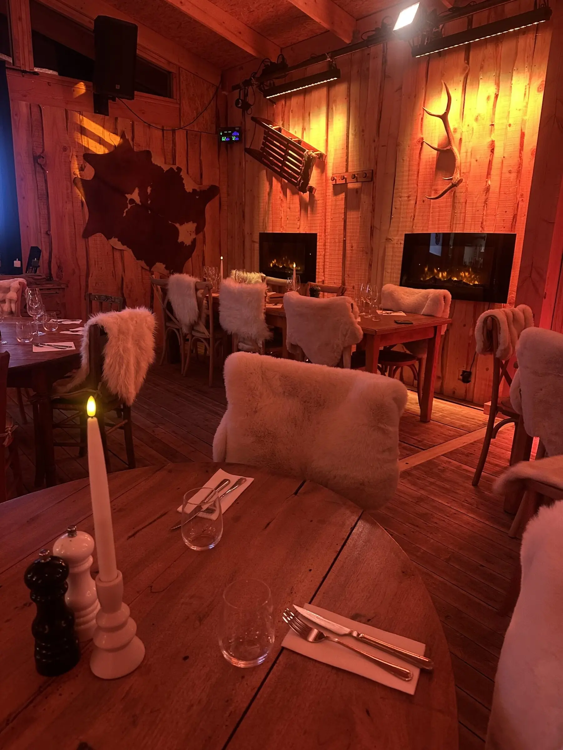 Table en bois dressée pour deux, chandelle allumée, cheminée et murs de planches en fond