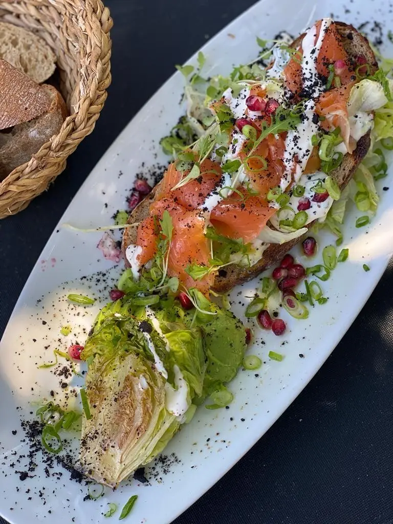 Tartine de saumon, crème, grains de grenade et pousses, cœur de laitue grillé, sur un plat long