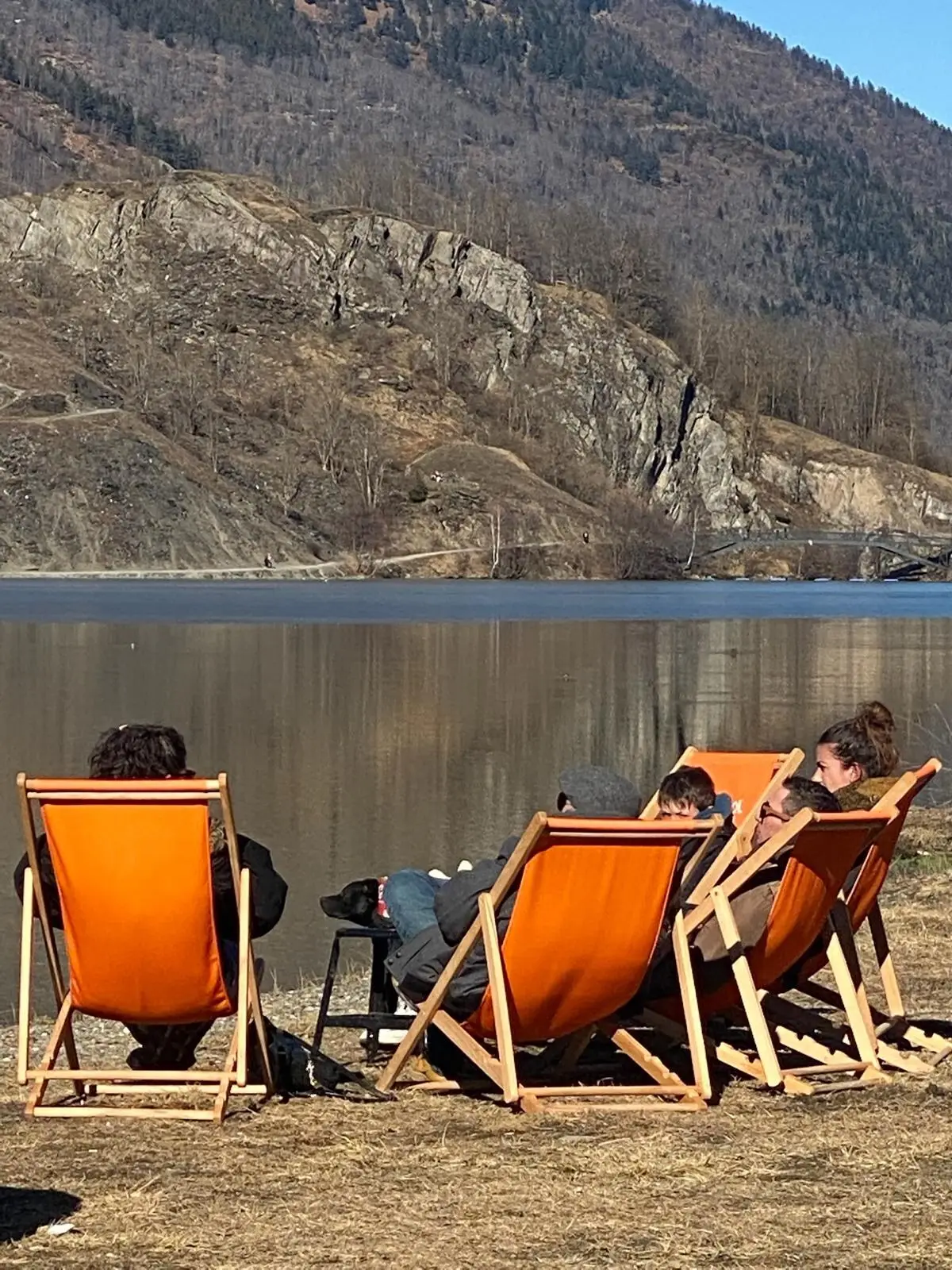 Transats orange alignés au bord du lac de Génos-Loudenvielle, face à la falaise, en fin d'hiver