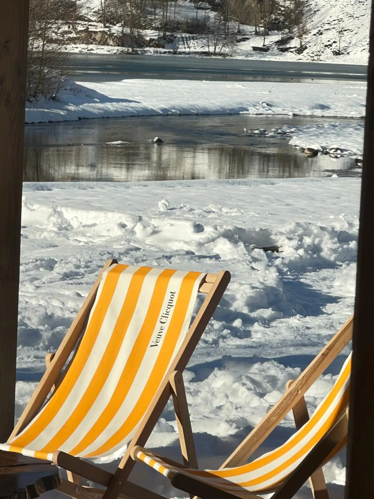 Deux transats rayés jaune et blanc posés dans la neige, face au lac de Génos gelé