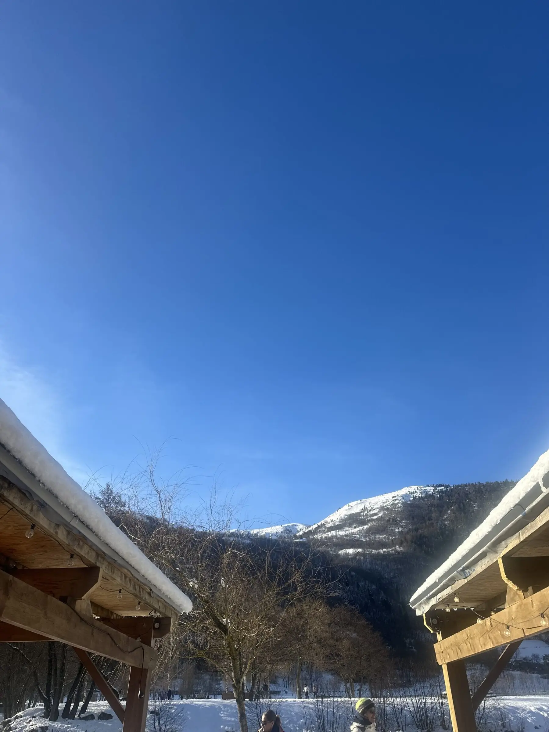 Vue depuis la terrasse couverte du chalet : montagnes enneigées sous un ciel bleu